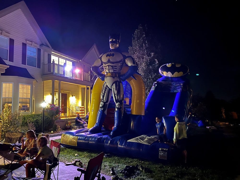 Batman-themed bounce house and slide combo lit up at a nighttime neighborhood party